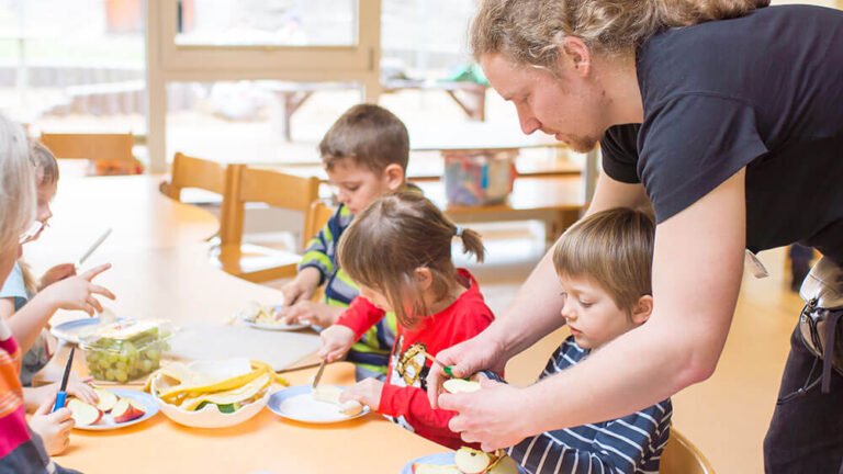 Ein Erzieher schneidet zusammen mit Kindern Obst