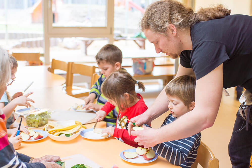 Ein Erzieher schneidet zusammen mit Kindern Obst