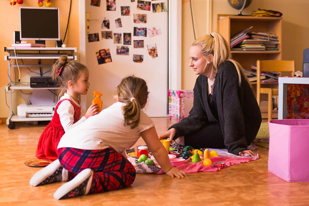 Eine Frau spielt mit zwei Kindern auf einer Pinknickdecke