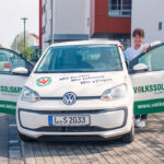 Eine Frau steht neben einem Auto, welches mit Werbung für die Volkssolidarität bedruckt ist