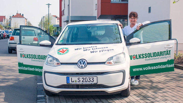 Eine Frau steht neben einem Auto, welches mit Werbung für die Volkssolidarität bedruckt ist