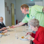 Ein Pfleger verteilt Essen an Senioren