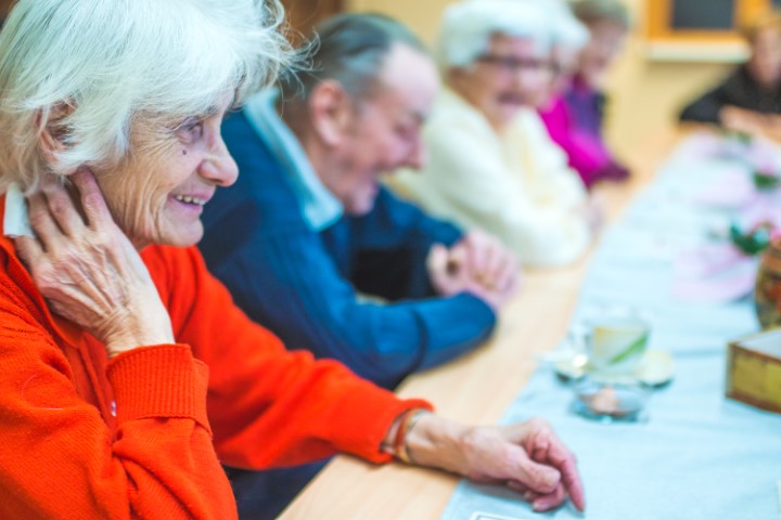 Zufriedene Seniorin sitzt mit anderen Senioren im Betreuten Wohnen beisammen.