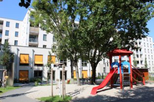 Rückansicht des Spielplatzes der Kindertagesstätte mit einer Rutsche und mehreren Klettergeräte