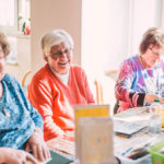 Drei Seniorinnen basteln gemeinsam; eine ist konzentriert, während die anderen beiden herzlich lachen.