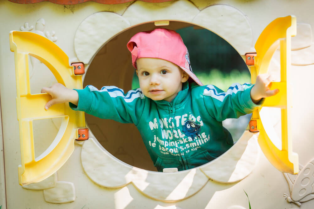 Kind schaut aus den offenen Fenstern eines Spielhauses hinaus