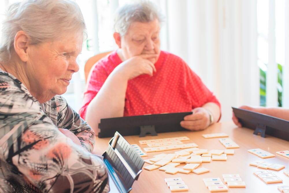 Zwei Senioren sind vertieft in ihr Rummikub-Spiel und spielen konzentriert.