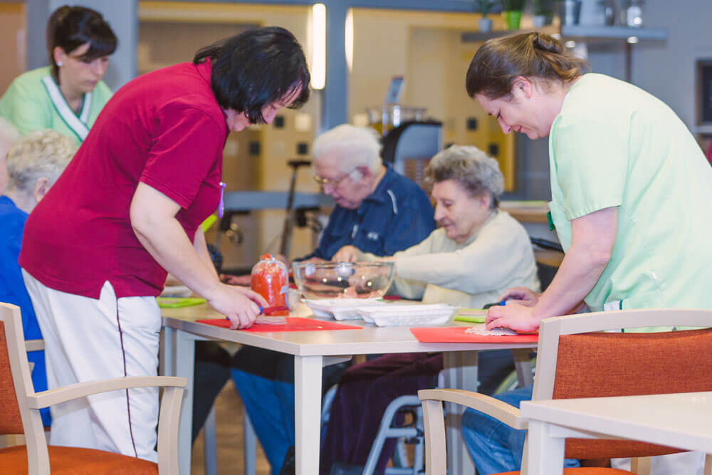 Pflegerinnen und Senioren bereiten gemeinsam Essen zu.