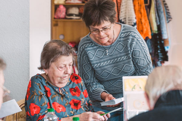 Ehrenamtliche Helferin und Seniorin schauen gemeinsam Grußkarte an.