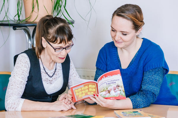 Zwei Frauen sitzen am Tisch und lesen gemeinsam ein Informationsheft.