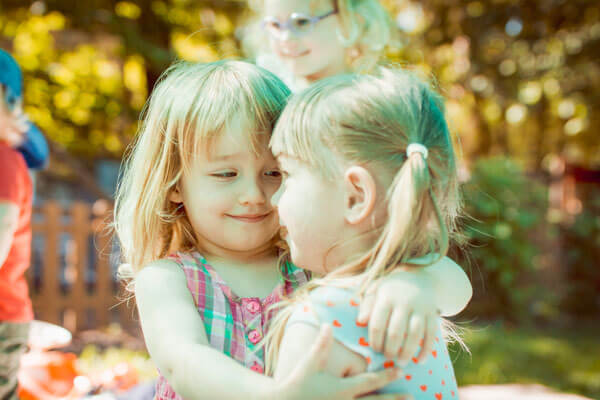 Kleines Mädchen umarmt ein anderes Mädchen und lächelt.